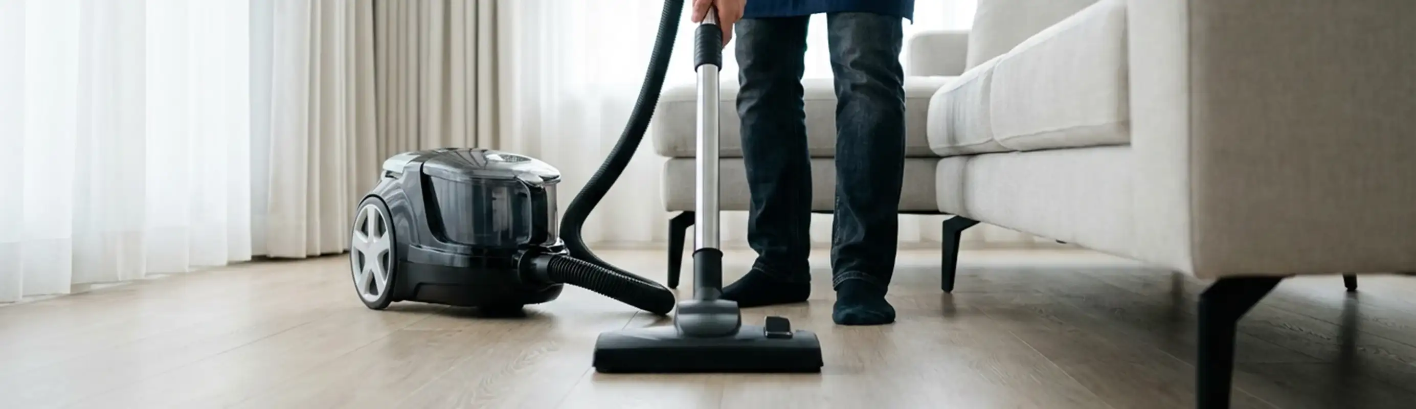 Professional house cleaner vacuuming a living room floor with a canister vacuum cleaner, Seattle, WA.
