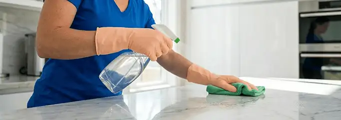 Maid service worker spraying and wiping a kitchen countertop with a microfiber cloth for sanitizing, Seattle, WA.
