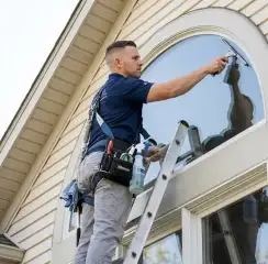 Professional window cleaner on a ladder using a squeegee to clean an exterior arched window, Seattle, WA.
