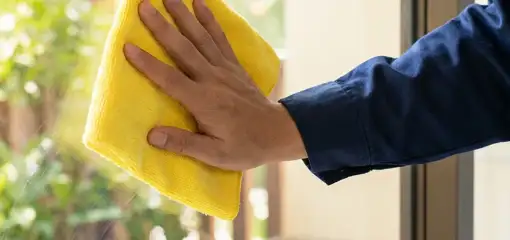 House cleaner wiping a glass window with a yellow microfiber cloth for streak-free cleaning, Seattle, WA.